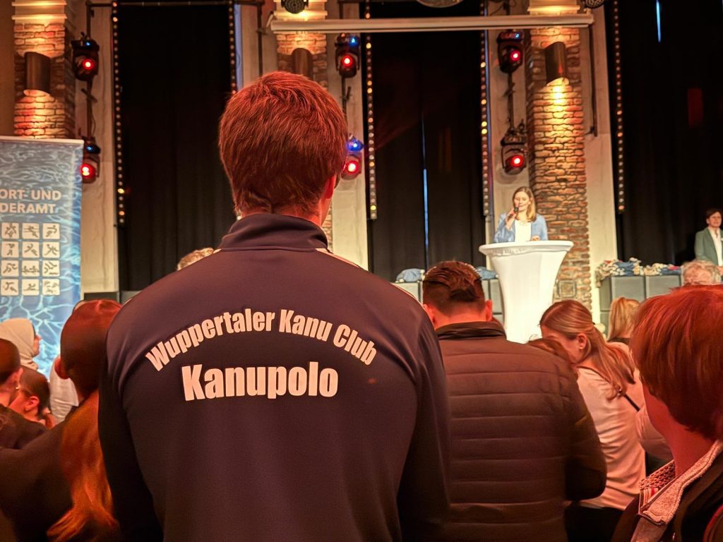 Lennarts von hinten fotografiert. Im Hintergrund eine Sprecherin auf einer Bühne